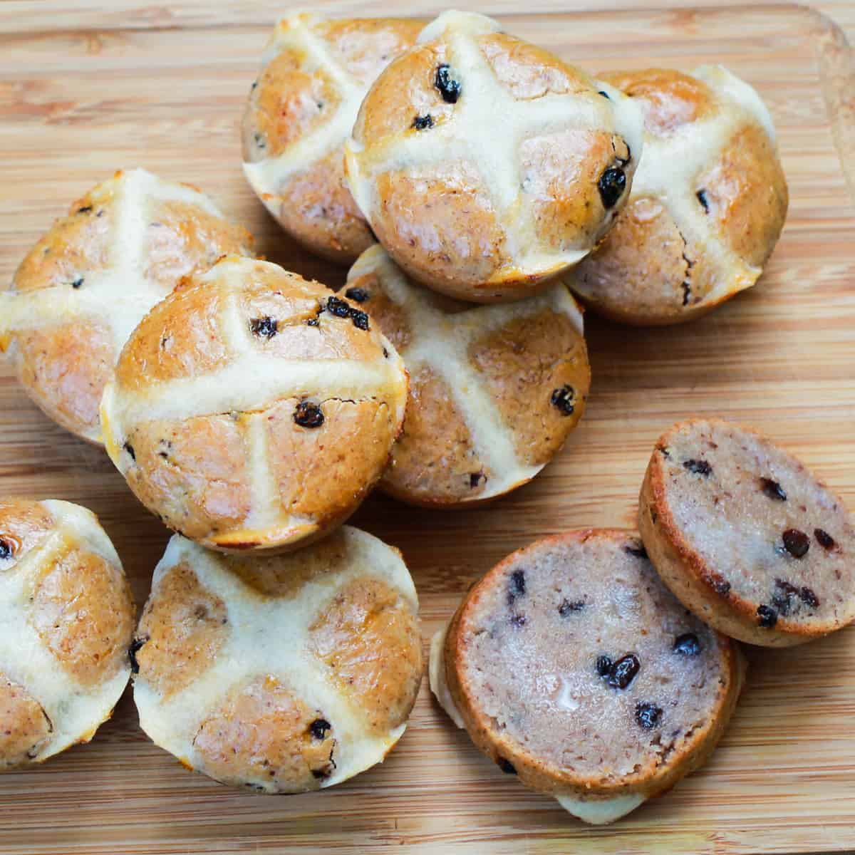 photo of hot cross buns piled onto a chopping board with one cut open and buttered.