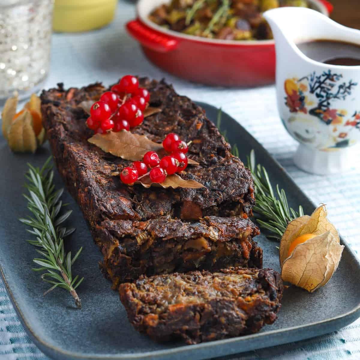 Photo of a chestnut nut roast garnished with redcurrants and fresh herbs and a jug of gravy.