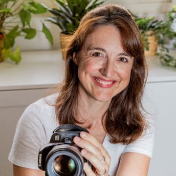 Square photo of Camilla Sanderson holding the camera and smiling with white cupboards and plants in the background.